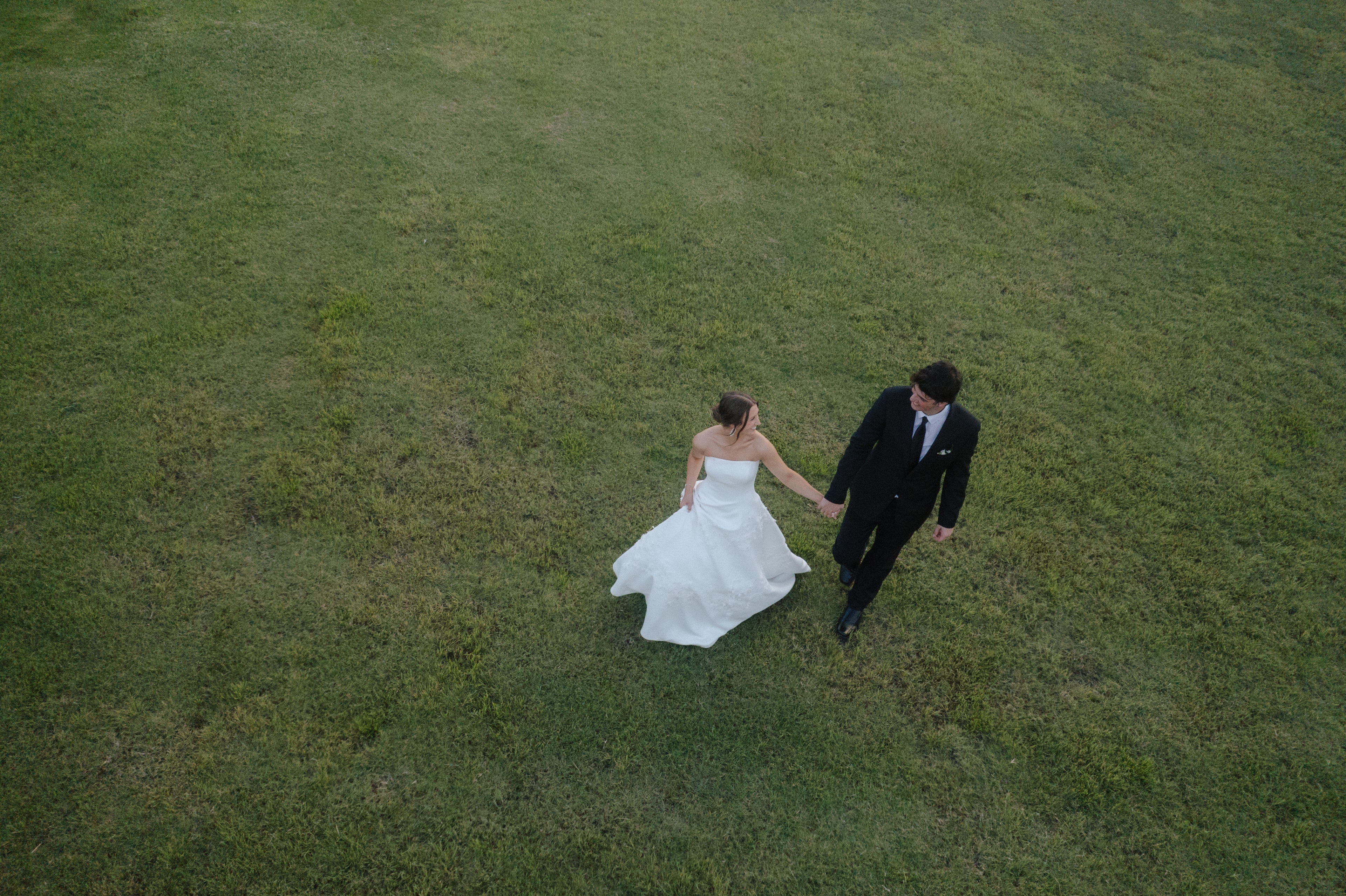 Aerial drone photo of Paige and DJ walking hand in hand across the green grounds of The French Farmhouse Venue
