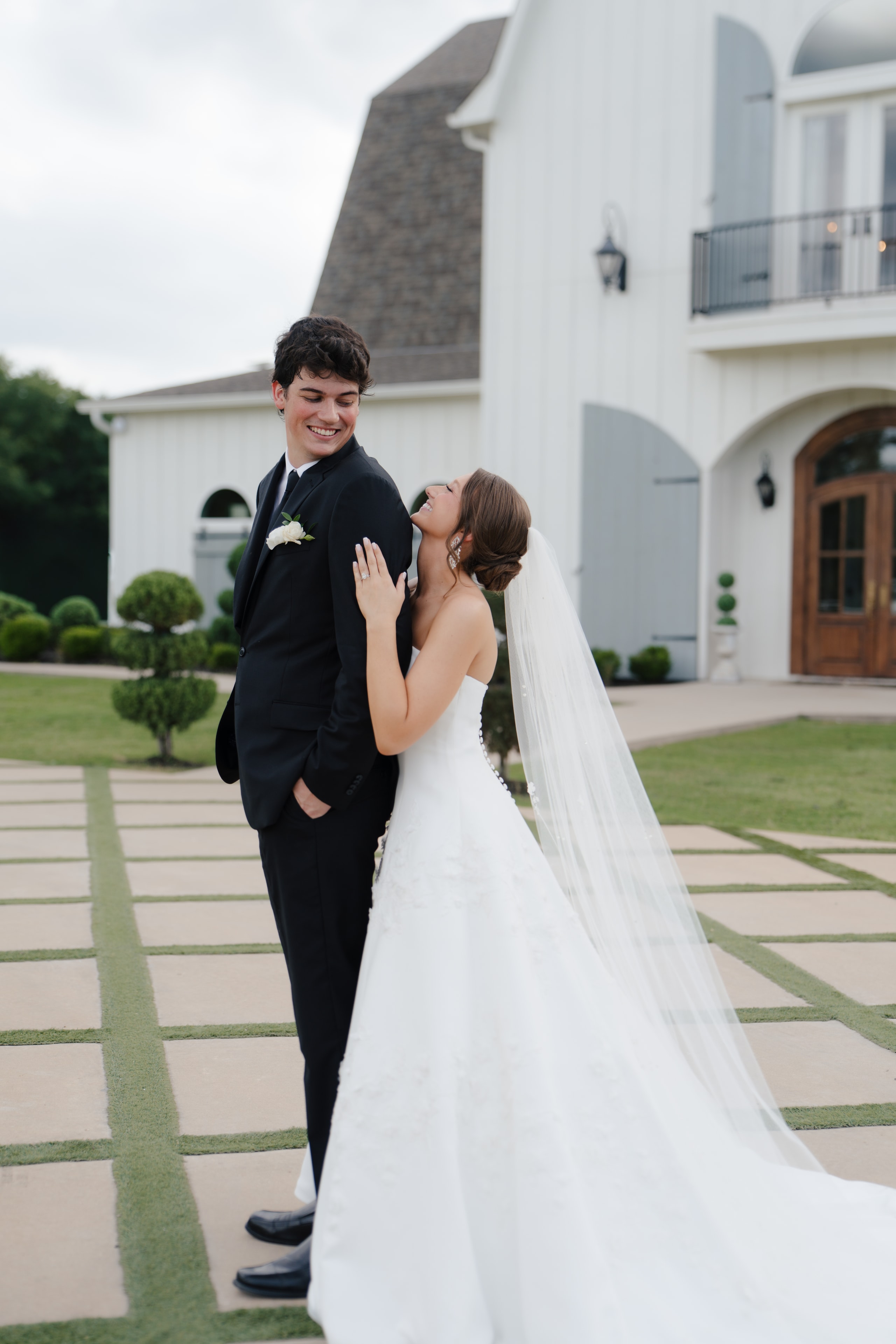 Paige and DJ laughing together in front of The French Farmhouse Venue entrance on their wedding day