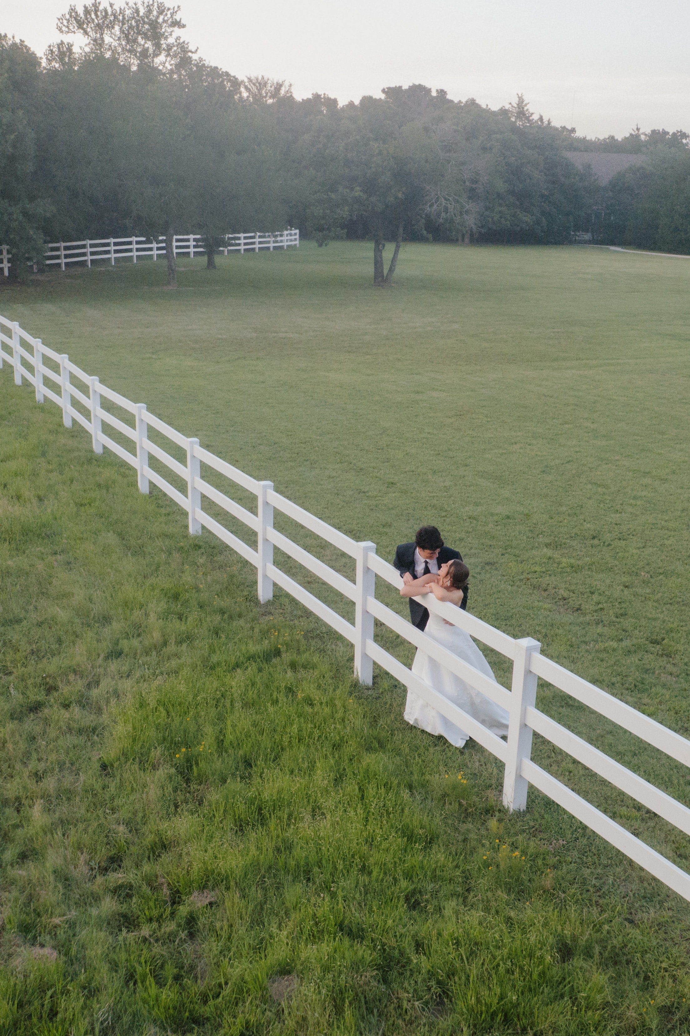 DJ dipping Paige for a kiss along the white fence at sunset on the grounds of The French Farmhouse Venue