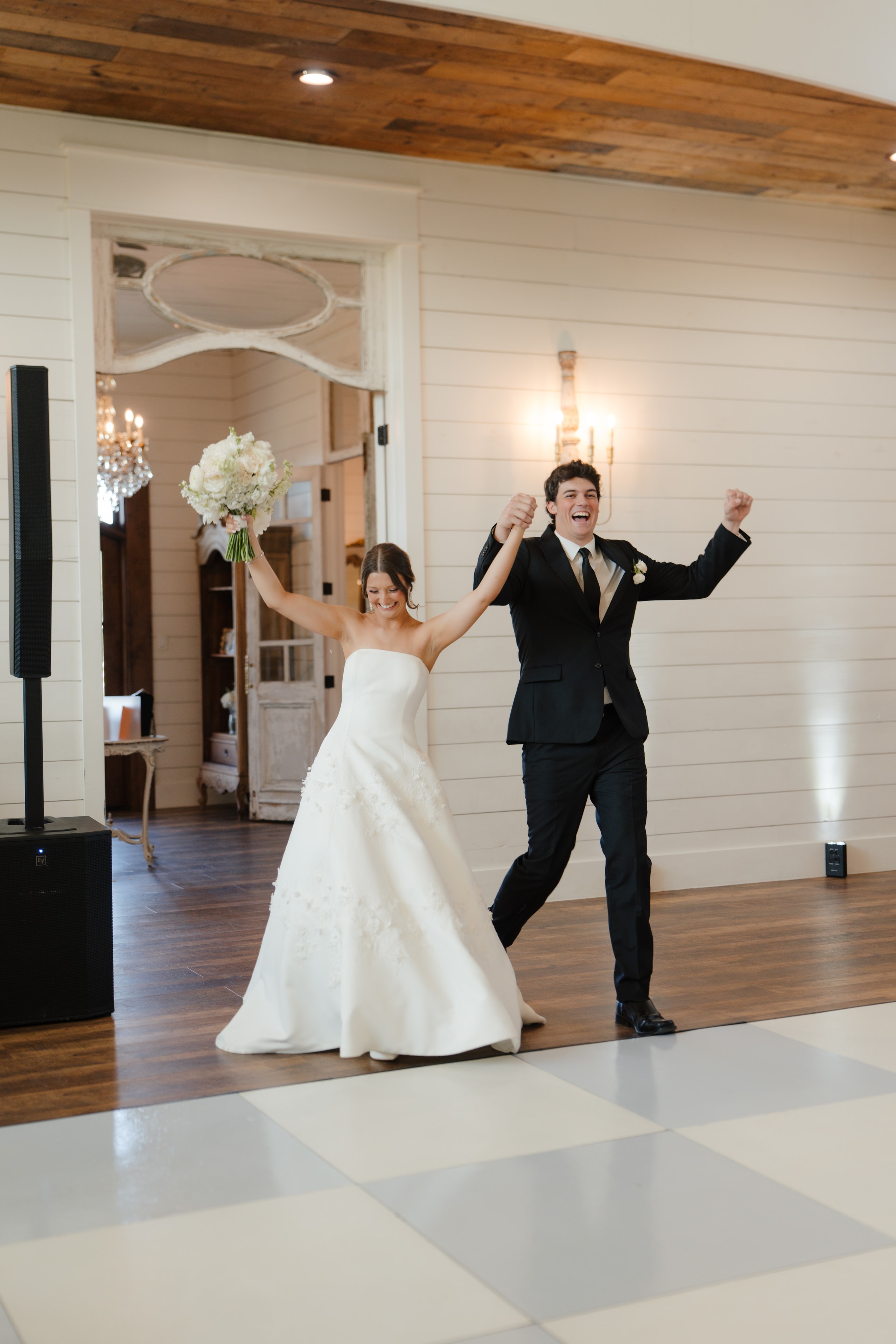 Paige and DJ making their grand entrance as newlyweds into the reception hall at The French Farmhouse Venue, arms raised in celebration