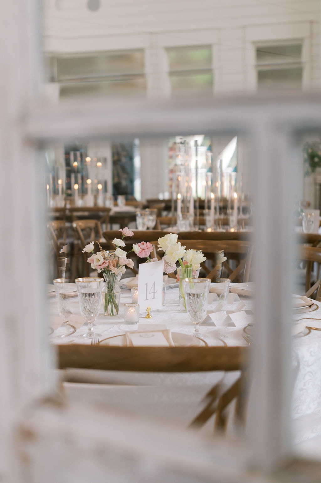 Shelby and Cole's floral escort card wall seating chart display at The French Farmhouse Venue — a lush arrangement of blush, peach, and cream garden roses, ranunculus, and greenery with individual wooden escort card picks tucked into the blooms, each bearing a guest's name and table number, the entire display mounted on a white lattice frame with a 'Pick Your Seat' sign at the top
