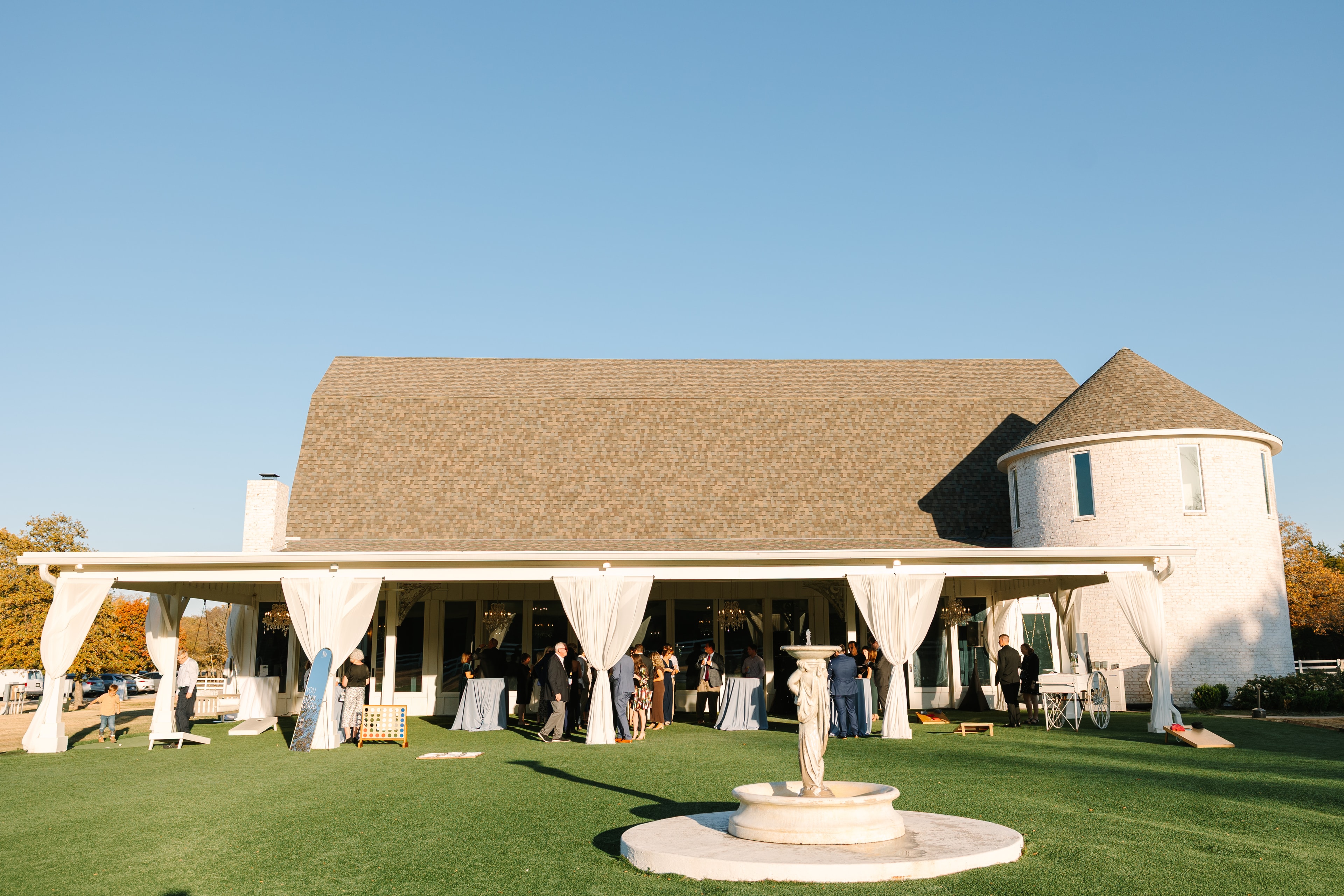 Wedding guests mingling on the lawn during cocktail hour with white draped pavilion, fountain, and the iconic silo at The French Farmhouse Venue