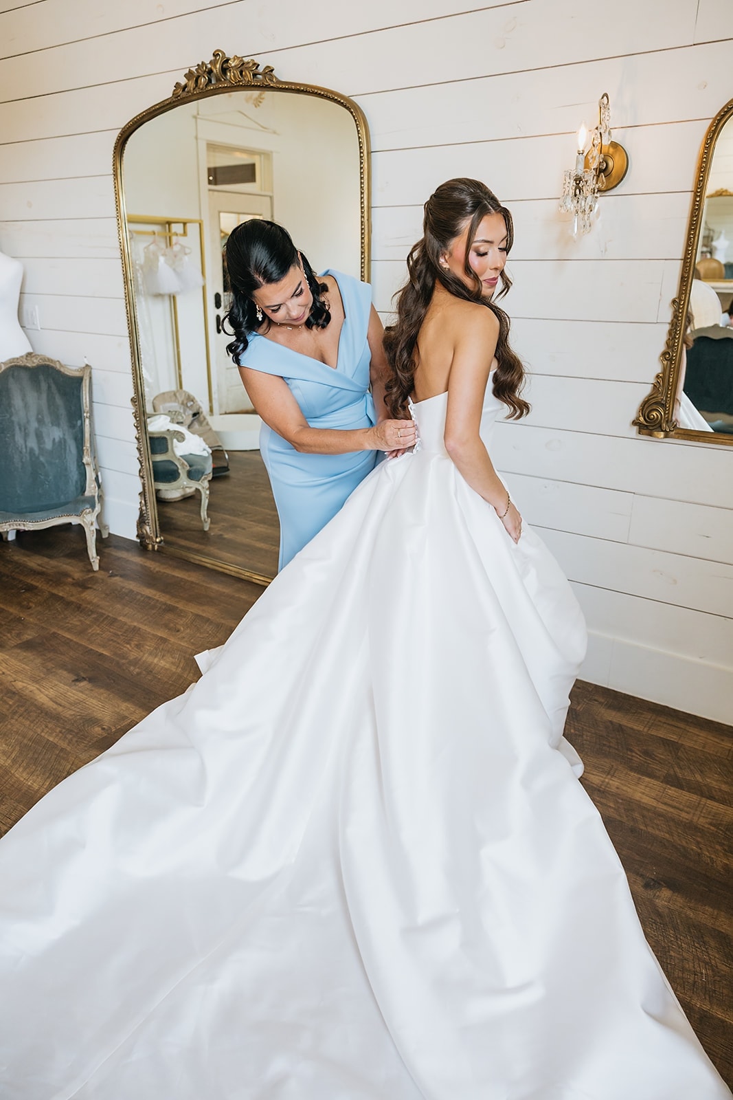 Bride celebrating with arms raised surrounded by bridesmaids in blue in the bridal suite