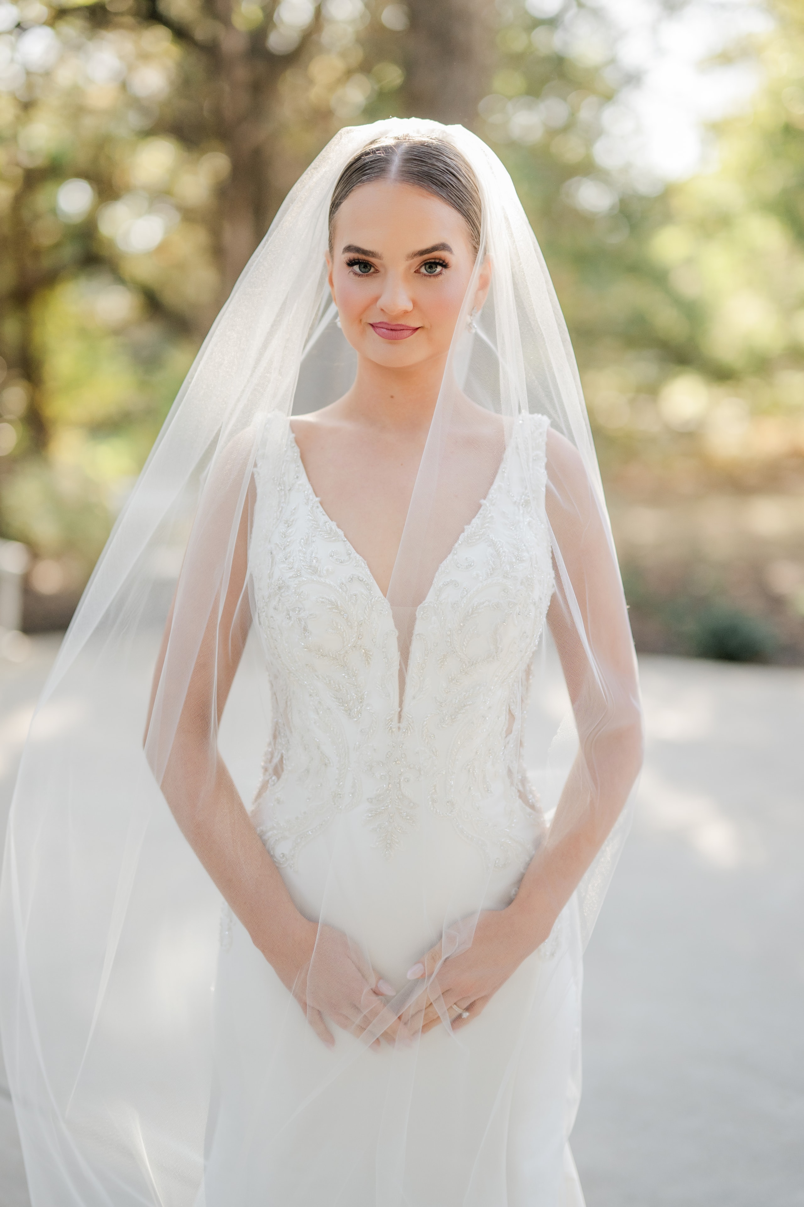 Bride in a beaded lace gown with cathedral veil posing outdoors on the grounds of The French Farmhouse Venue