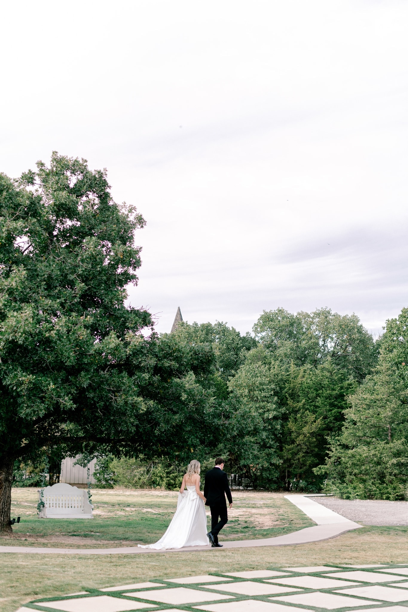 Couple walking the grounds at The French Farmhouse Venue with the chapel steeple in the background