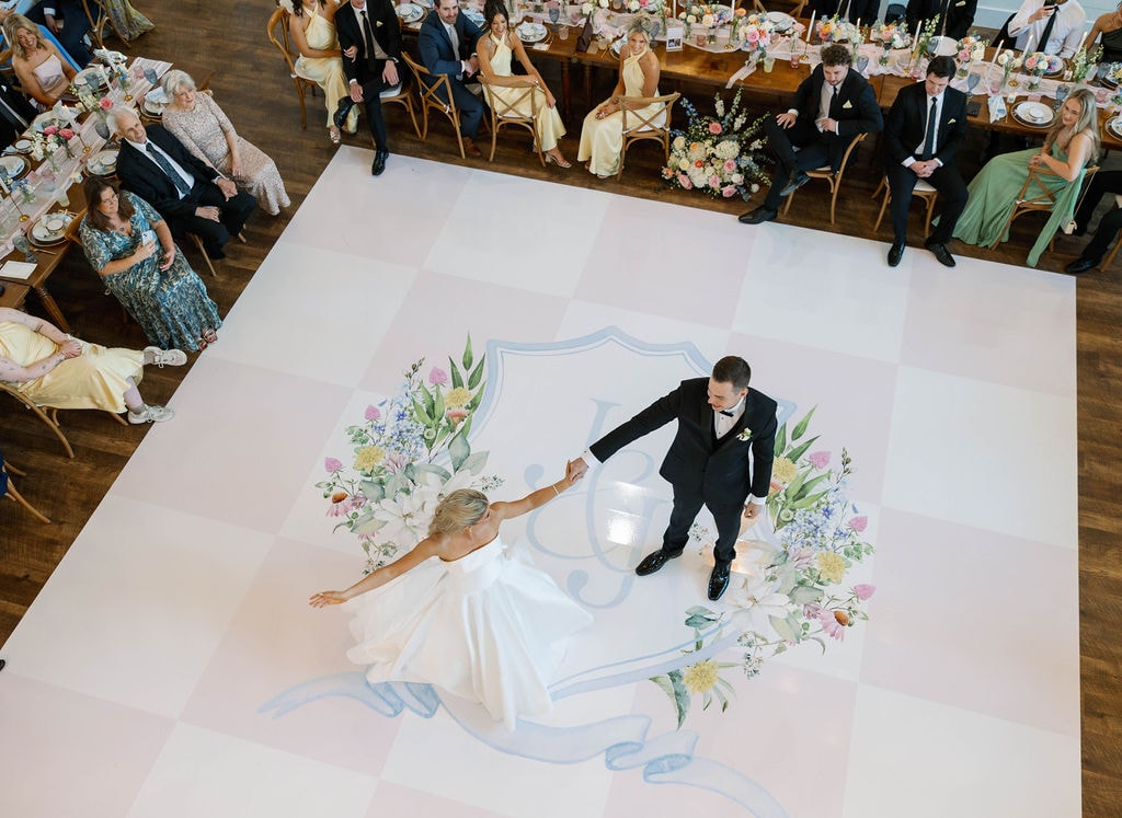 Bride and groom sharing their first dance on a custom painted monogram dance floor at The French Farmhouse Venue