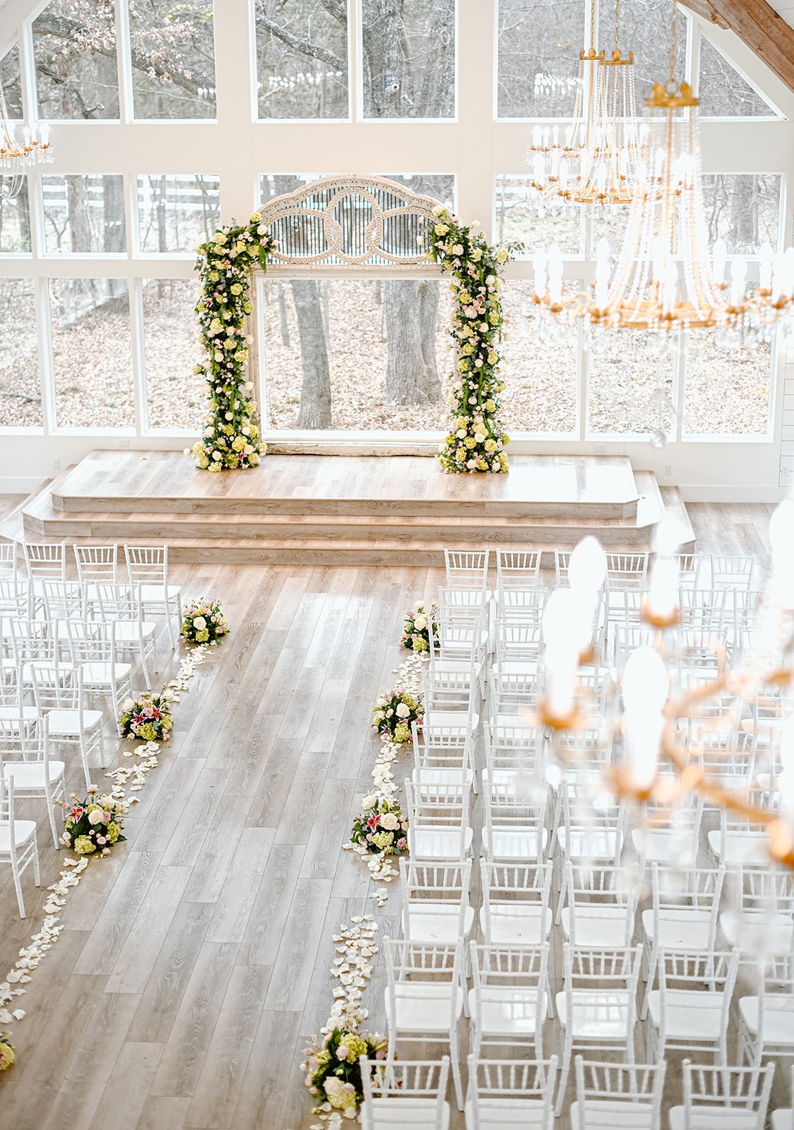 Elegant reception hall interior with floral arch, white chiavari chairs, and rose petal aisle at The French Farmhouse Venue