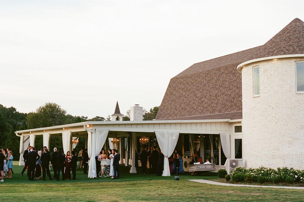 Wedding guests mingling on the covered patio at The French Farmhouse Venue at golden hour