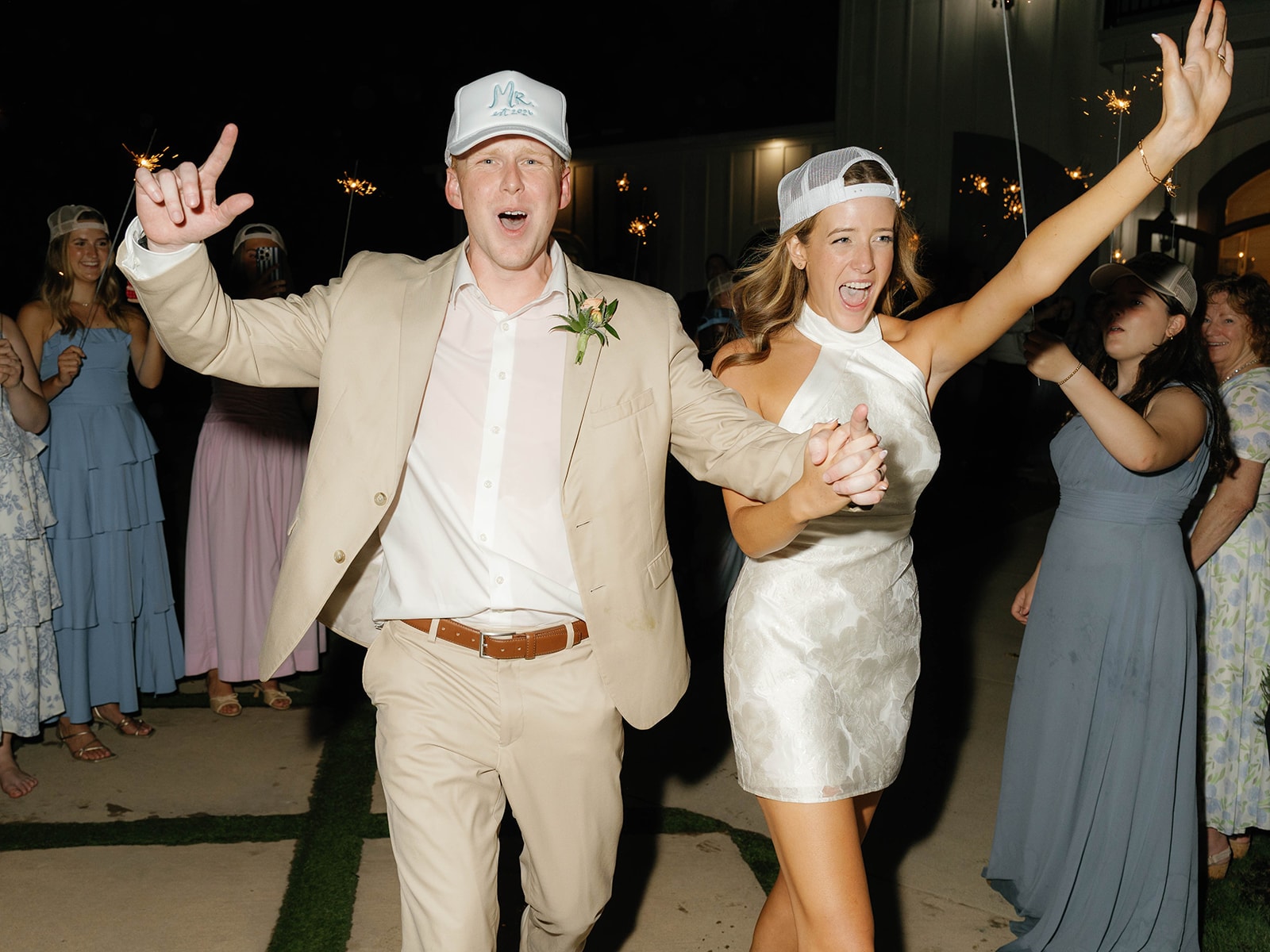 Newlyweds celebrating with sparklers and guests outside The French Farmhouse Venue at night
