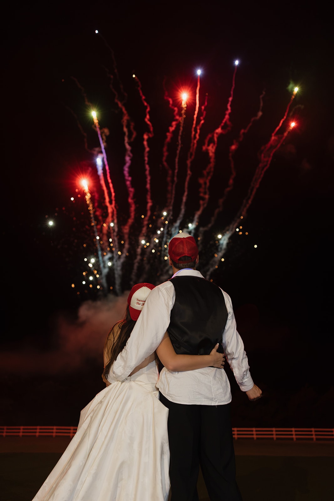Nina and Gage Jackson in their 'Forever Ever The Jacksons' trucker hats watching Dallas Elevate fireworks light up the Texas sky on their 4th of July wedding night at The French Farmhouse Venue