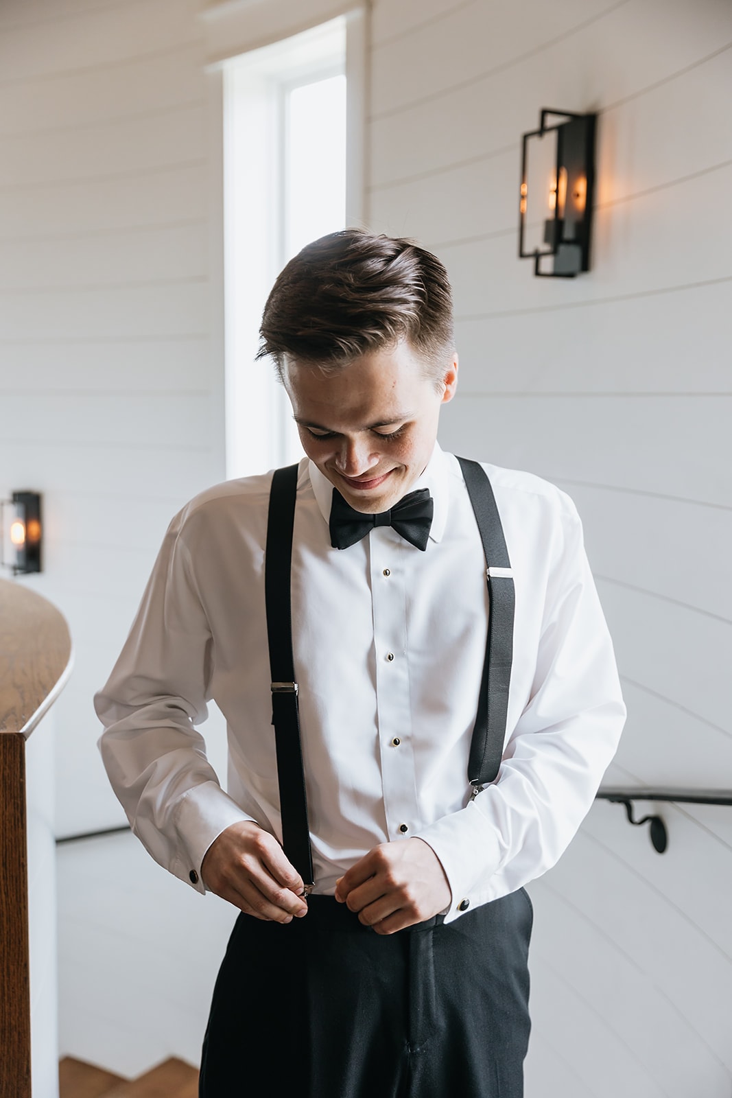 Groom in white shirt and black suspenders smiling on the spiral staircase